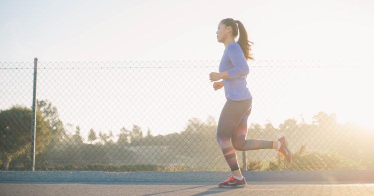 Woman running on road at dusk in front of a chain link fence