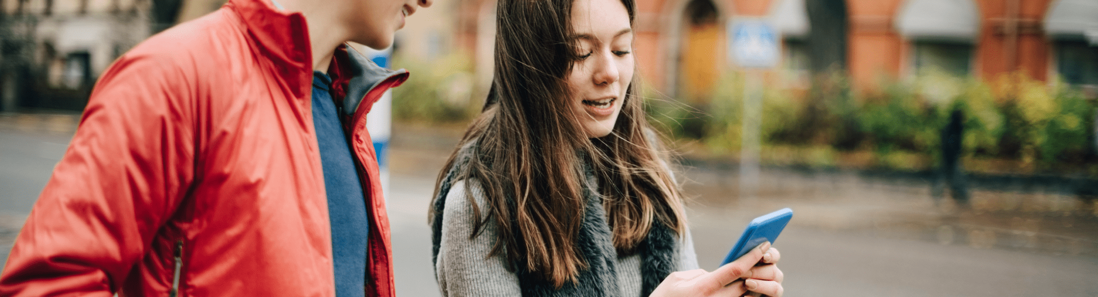 Teenage boy and girl walking and talking while looking at a smartphone