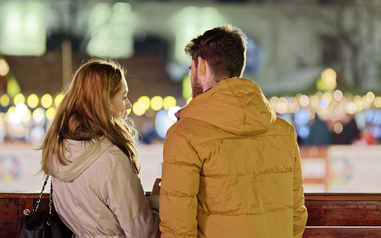 A young couple wearing jackets standing with their backs facing the camera