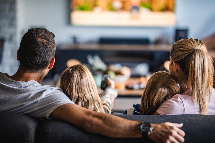 Back view of a relaxed family watching TV on sofa in the living room.