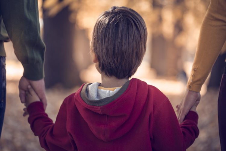 Boy holding his parents hands in public park