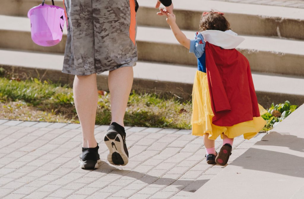 Child dressed as snow white holding father's hand while trick or treating on halloween