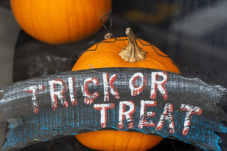 Orange pumpkin with a wooden sign reading "Trick or Treat" hung over its stem