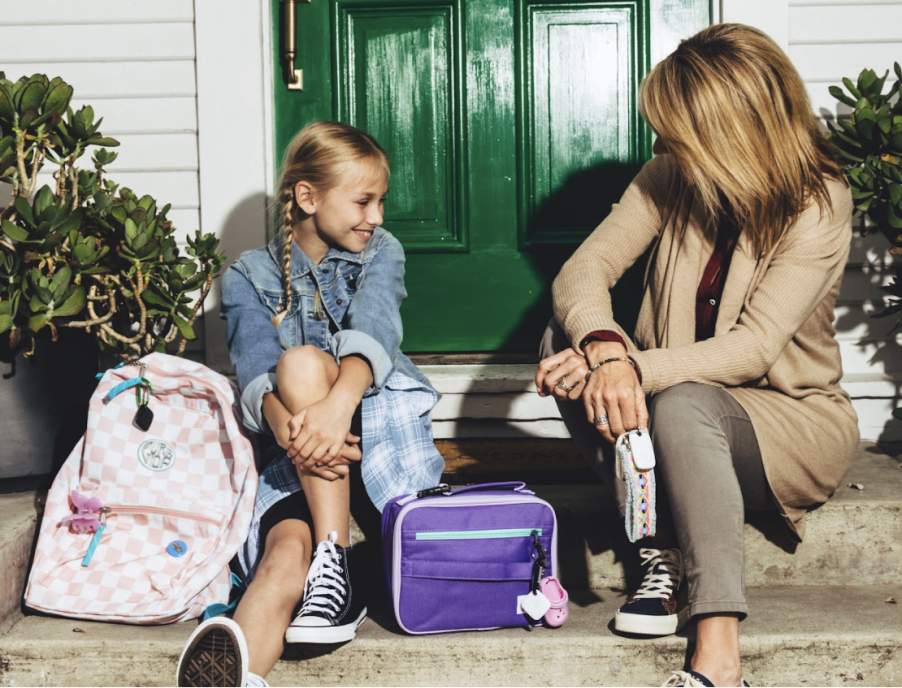 A mother and daughter sitting on their front porch next to the daughter's backpack and lunchbox.