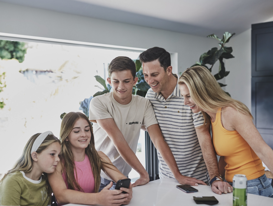 A family of five standing around a phone at a kitchen counter.