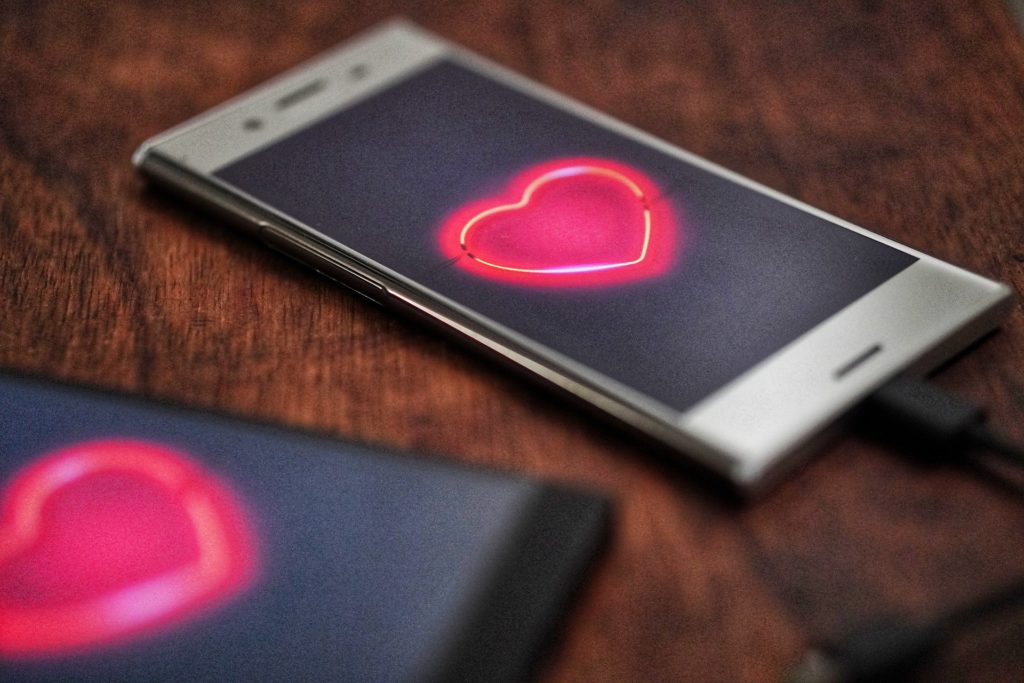 Two android smart phones next two each other with red neon hearts on the screens
