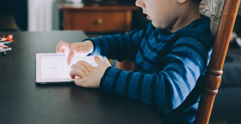 A young boy sitting at a table playing on a tablet