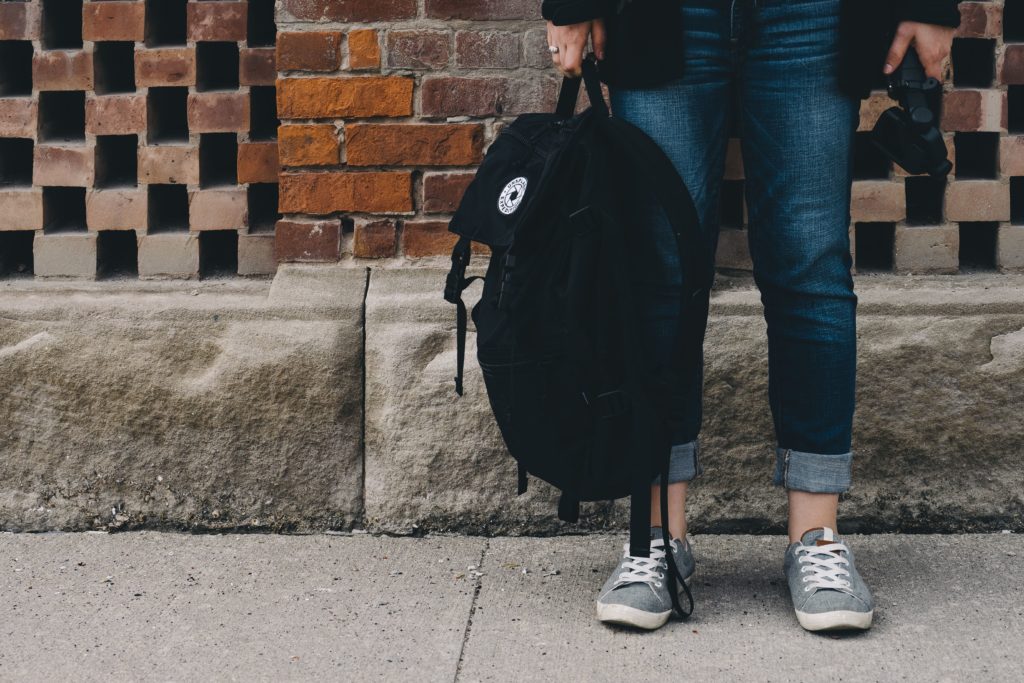 Child standing on sidewalk holding a backpack