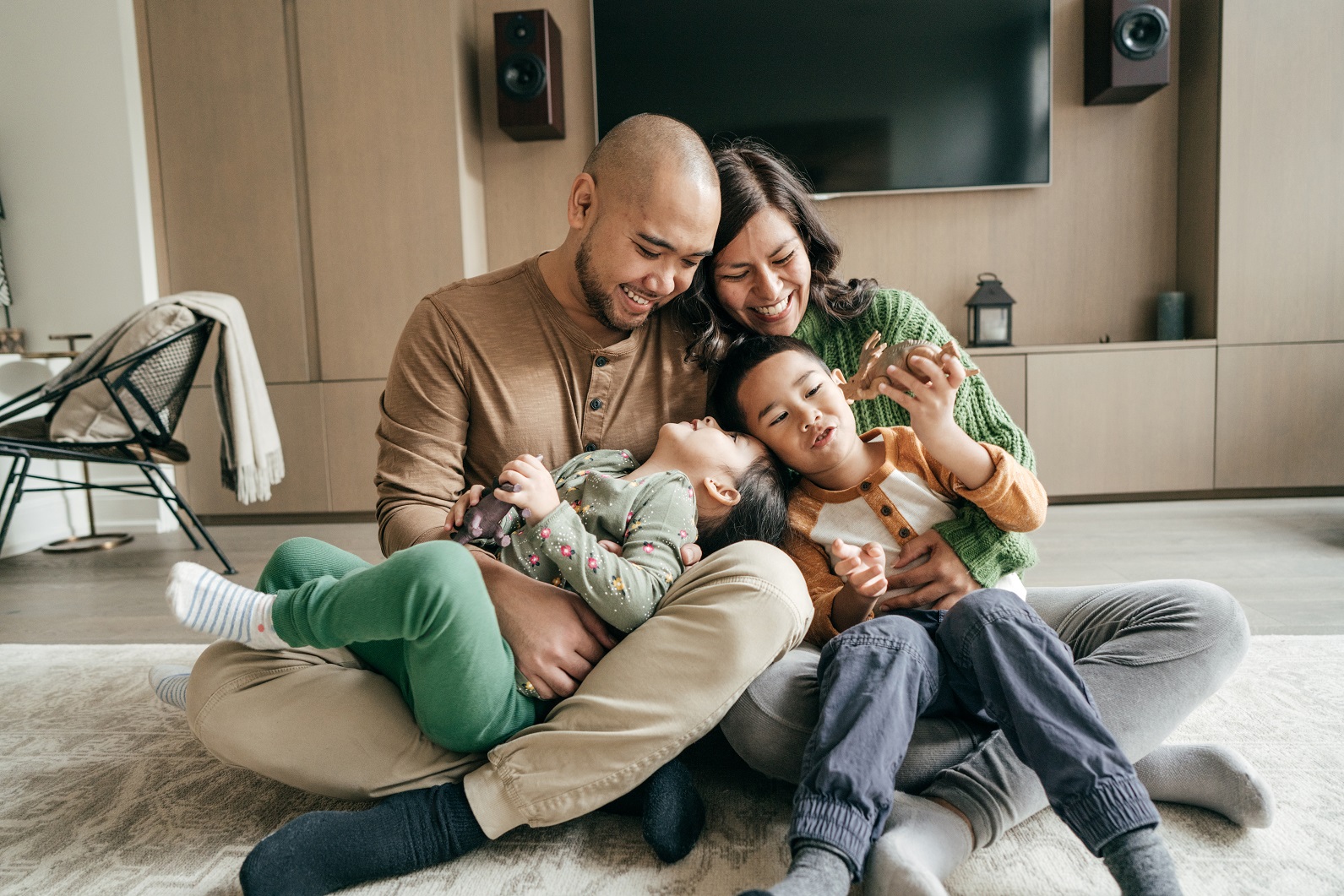 4 person family laughing and cuddling while sitting in their living room on the floor